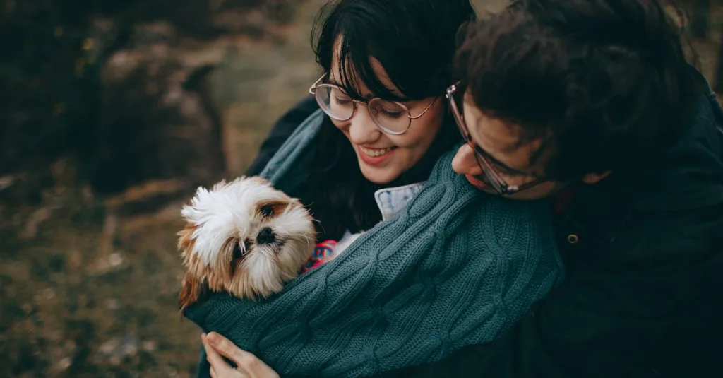 A happy couple cuddles their Shih Tzu dog outdoors, showcasing love and joy.