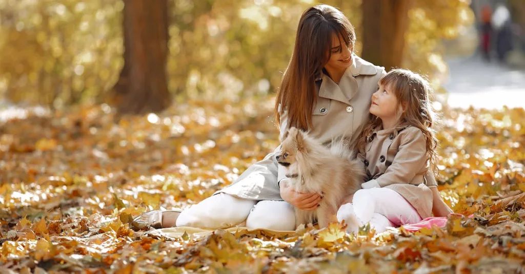 Mother and daughter with a dog enjoying a sunny autumn day in the park.